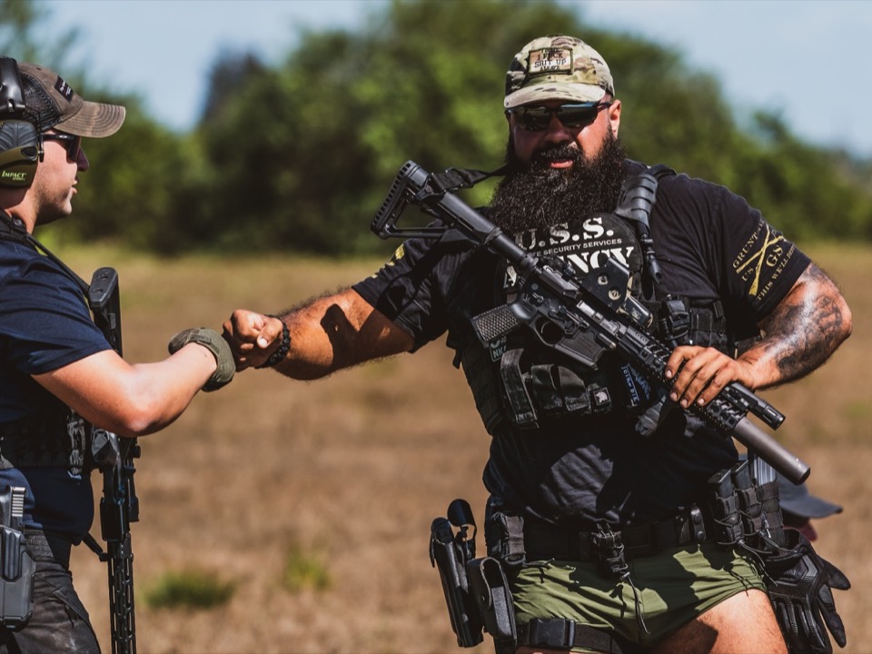 Two USS Academy tactical operators fist-bumping at outdoor training field showing team camaraderie