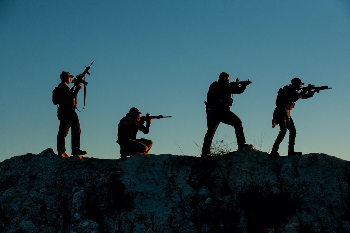 Four USS Academy instructors silhouetted on ridge at sunset with rifles in tactical formation